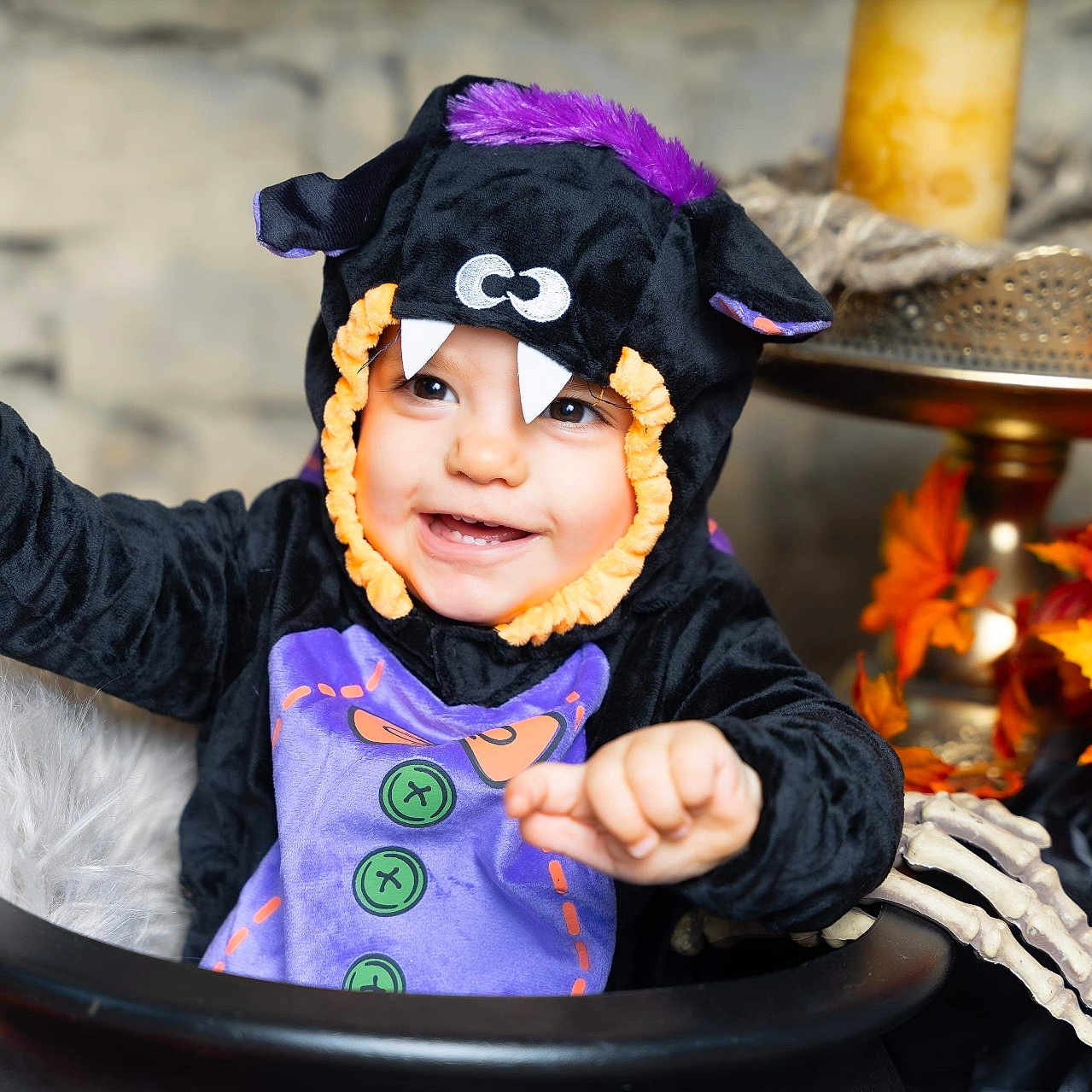 Mia participe au concours pour gagner de l'argent avec cette photo : autumn_leaves, black_clothing, cauldron, celebration, child, costume, cute, decorations, face, festive, halloween, hand, happy, holiday, indoor, monster, playful, purple, smile, toddler