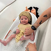 Rowan joined the competition — help win amazing prizes! baby, bathtub, bubbles, child, foam, hand, hat, infant, person, skin, tattoo, water, wash, yellow_cloth, bath, bathroom, cute, smile, sitting, adult