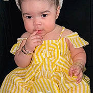 Kiari is registered to the contest to win money with this photo: child, toddler, bunny_ears, yellow_dress, striped_dress, sitting, indoor, bracelets, curly_hair, footwear, white_sandals, black_couch, cute, adorable, portrait, baby, headband, fashion, childhood, pensive