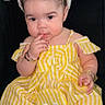 child, toddler, bunny_ears, yellow_dress, striped_dress, sitting, indoor, bracelets, curly_hair, footwear, white_sandals, black_couch, cute, adorable, portrait, baby, headband, fashion, childhood, pensive