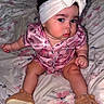 Kiari joined the competition — help win amazing prizes! baby, infant, child, headband, bow, pink_clothing, sitting, bed, blanket, floral_pattern, slippers, cute, indoors, portrait, curly_hair, expression, person, soft_lighting, cozy, fashion