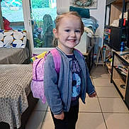 Mayanna participe au concours pour gagner de l'argent avec cette photo : backpack, buddha_art, casual_clothing, child, couch, decor, door, furniture, girl, happy, household_items, indoor, person, shelves, shoes, smiling, standing, tiled_floor, window, young_child