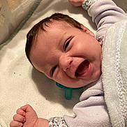 Luna is registered to the contest to win money with this photo: baby, infant, smiling, laughing, blanket, pacifier, crib, cute, newborn, face, mouth_open, eyes_squinting, onesie, arm, hand, lying_down, portrait, close_up, soft_texture, happy