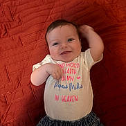 Luna joined the competition — help win amazing prizes! baby, smiling, infant, clothing, white_shirt, denim_pants, red_blanket, lying_down, happy, cute, portrait, child, one_person, casual, text_on_shirt, indoor, playful, young_child, baby_girl, relaxed