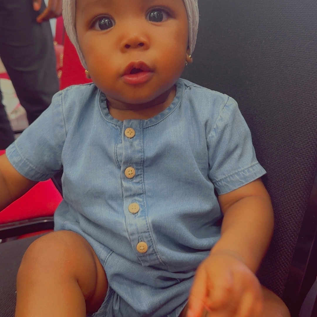 Eldrianna joined the competition — help win amazing prizes! baby, black_chair, buttons, chair, child, curious, cute, denim_romper, expression, eyes, face, footwear, hand, headwrap, indoor, person, portrait, sitting, skin, young_child