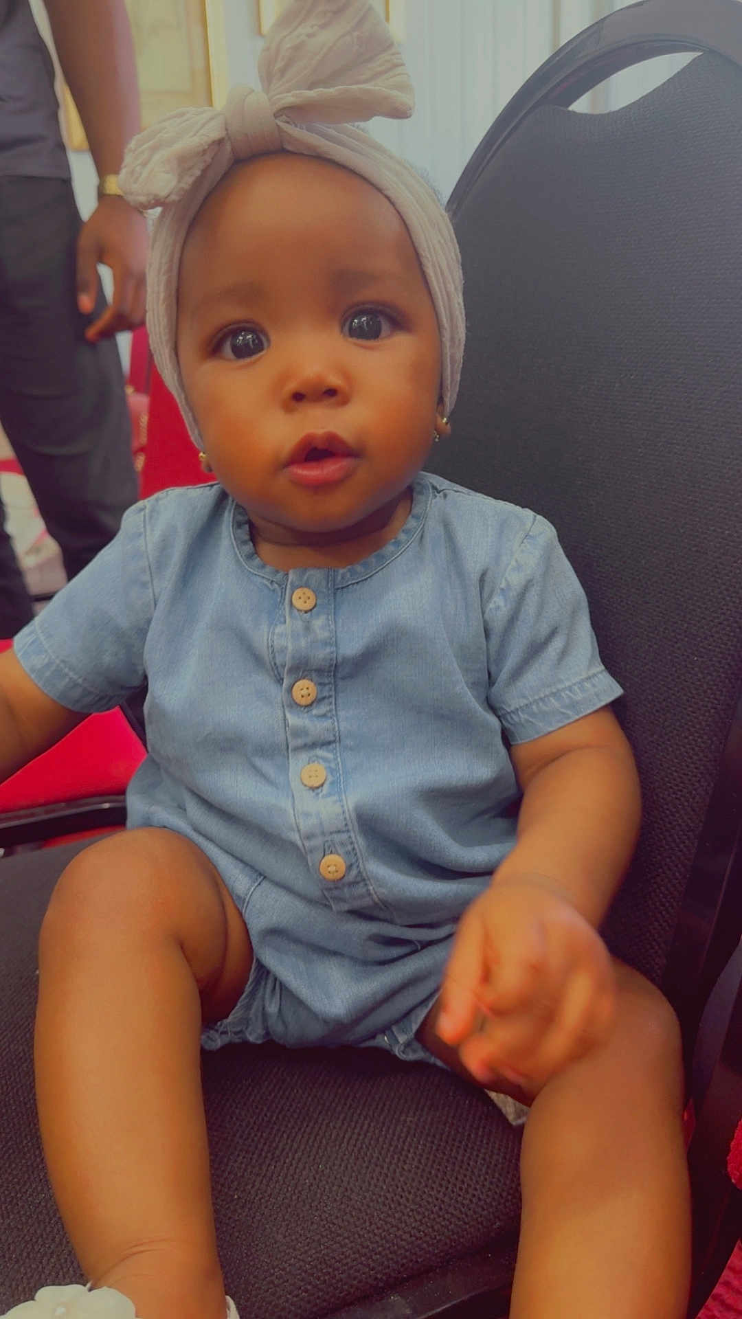 Eldrianna joined the competition — help win amazing prizes! baby, child, denim_romper, headwrap, chair, indoor, curious, sitting, cute, portrait, person, black_chair, buttons, footwear, skin, hand, face, eyes, expression, young_child