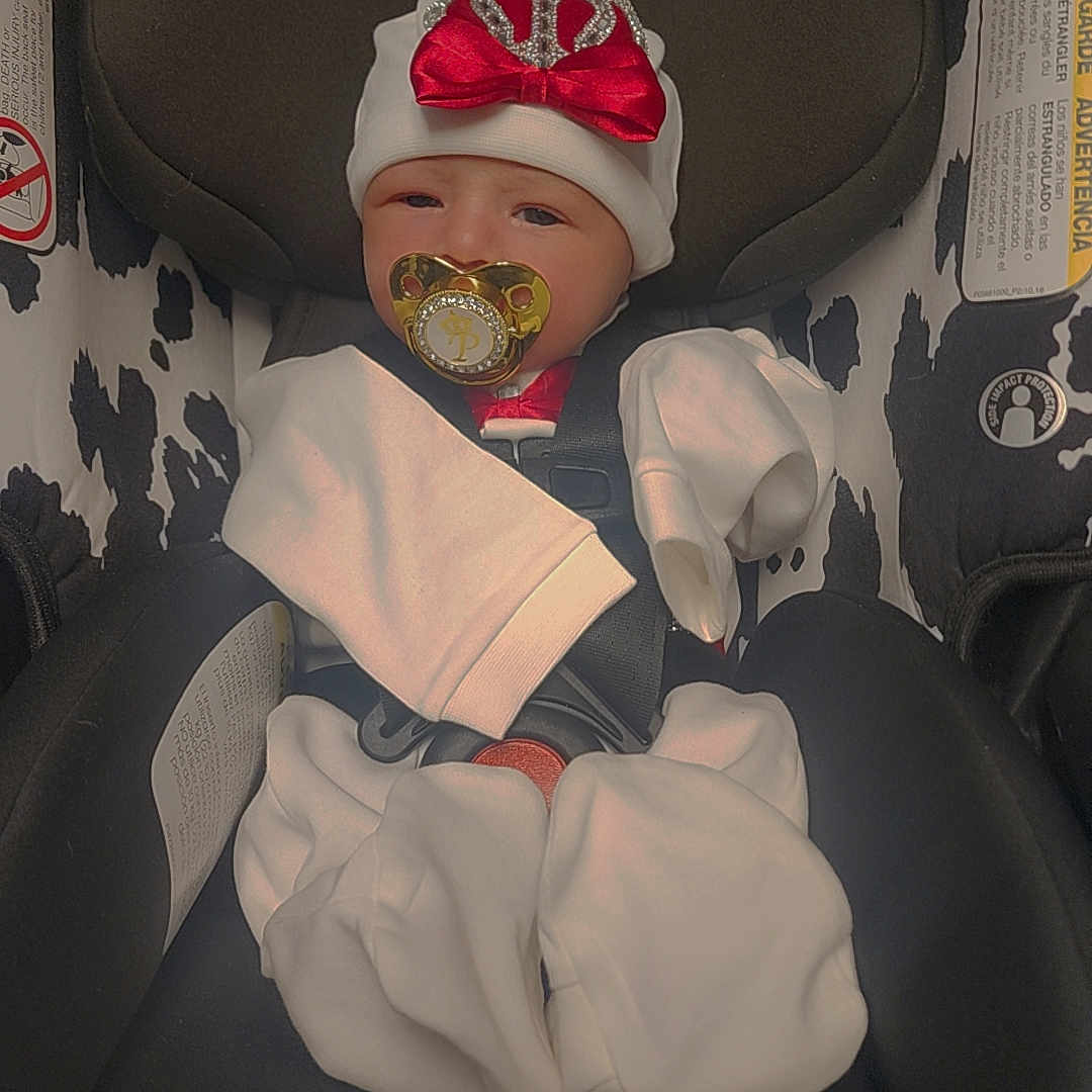 Princeten is registered to the contest to win money with this photo: baby, pacifier, car_seat, infant, hat, bow, clothing, white_clothes, black_and_white, pattern, child, seatbelt, newborn, cute, indoors, portrait, sitting, resting, headwear, small_baby