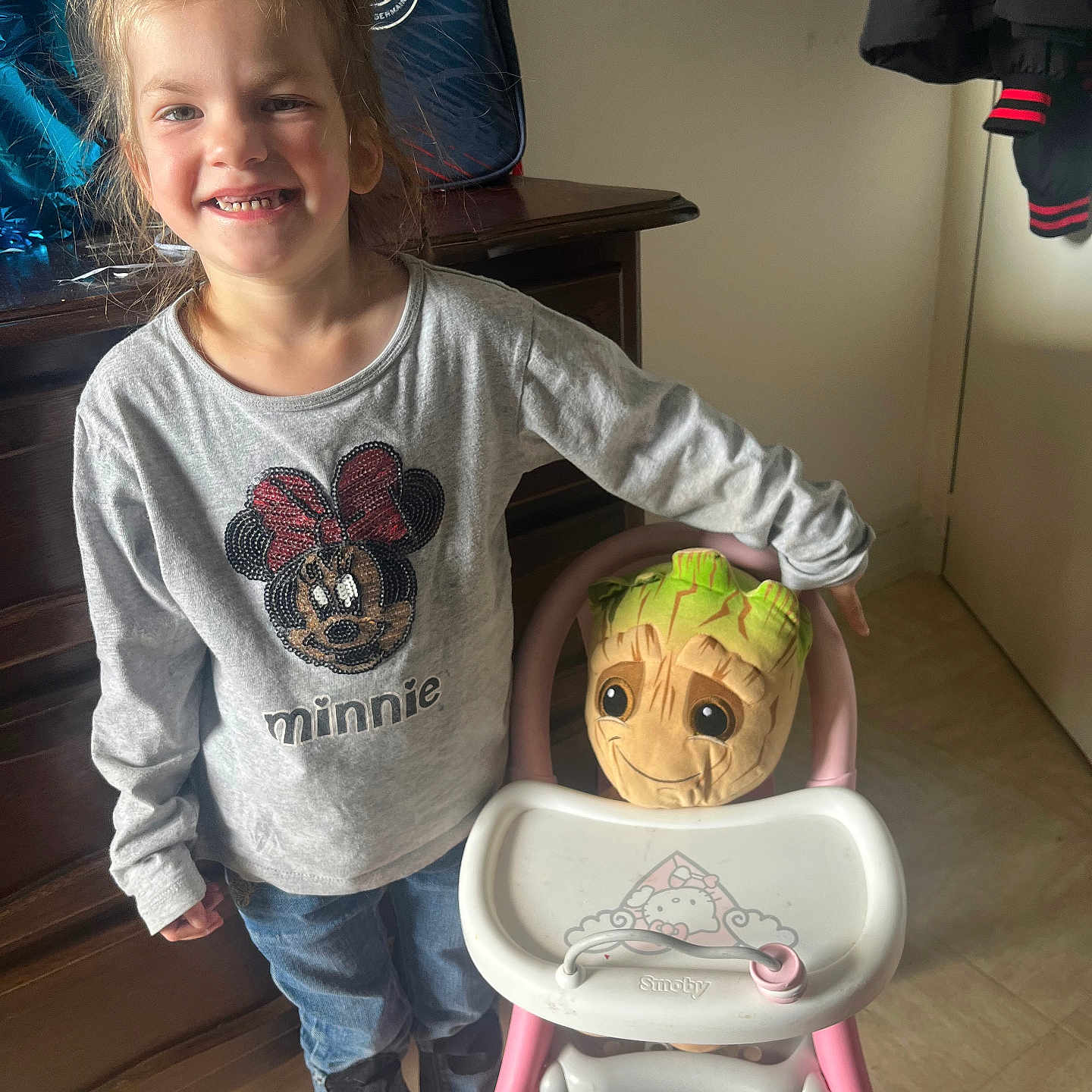 Lennzy a rejoint le concours — aidez-le/la à gagner de superbes lots ! casual_clothing, child, cute, flooring, girl, hair, happy, high_chair, indoor, jeans, minnie_mouse, person, pigtails, playful, plushie, smile, standing, sweatshirt, toy, wooden_furniture