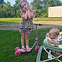 child, baby, girl, scooter, walker, grass, outdoor, play, leopard_print, shorts, shoes, headband, pout, pose, summer, daylight, curious, greenery, toys, fun