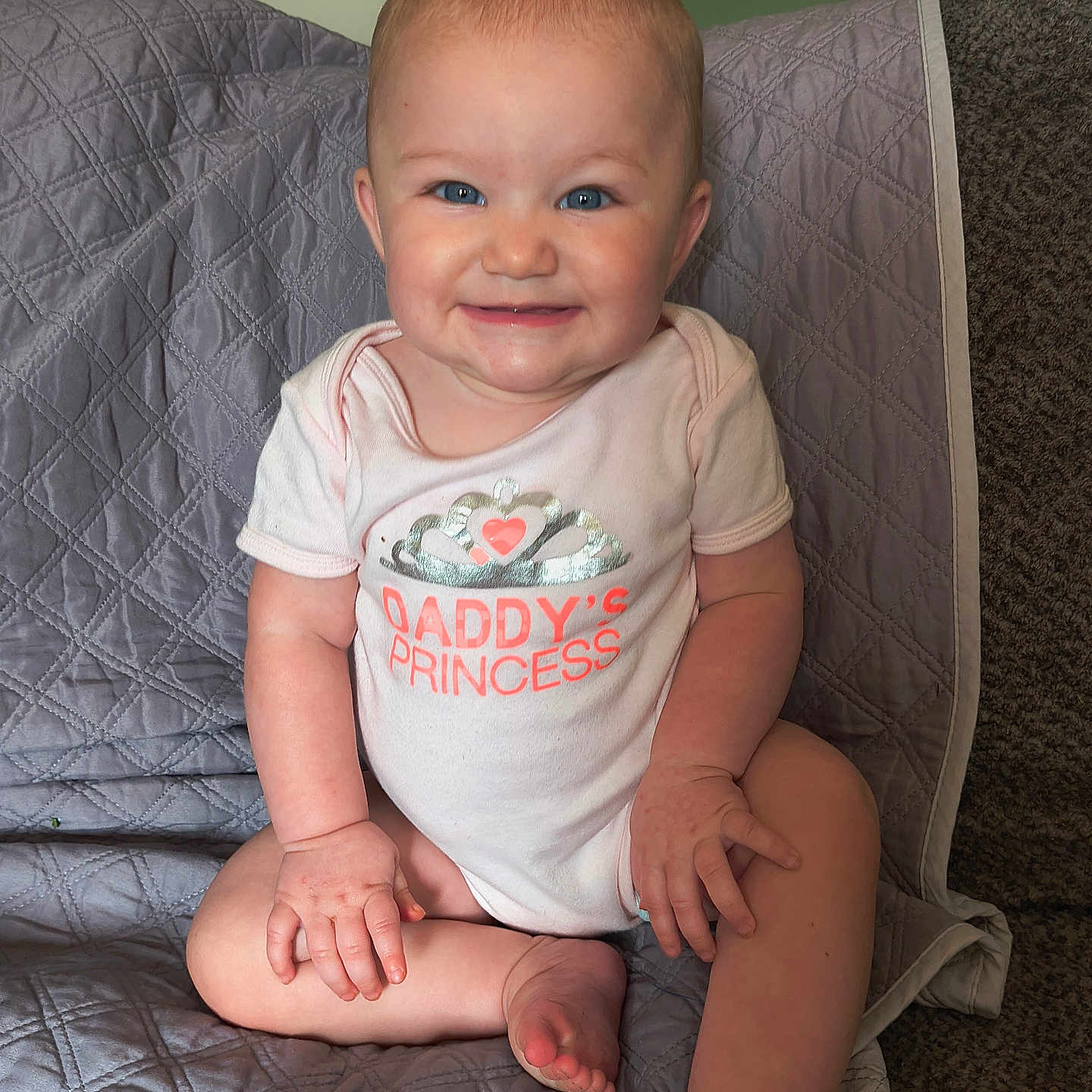 Harley is registered to the contest to win money with this photo: baby, blue_eyes, candid, child, cute, daddys_princess, face, feet, gray_blanket, hands, happy, indoors, infant, onesie, portrait, quilted_blanket, sitting, skin, smile, tiara_graphic