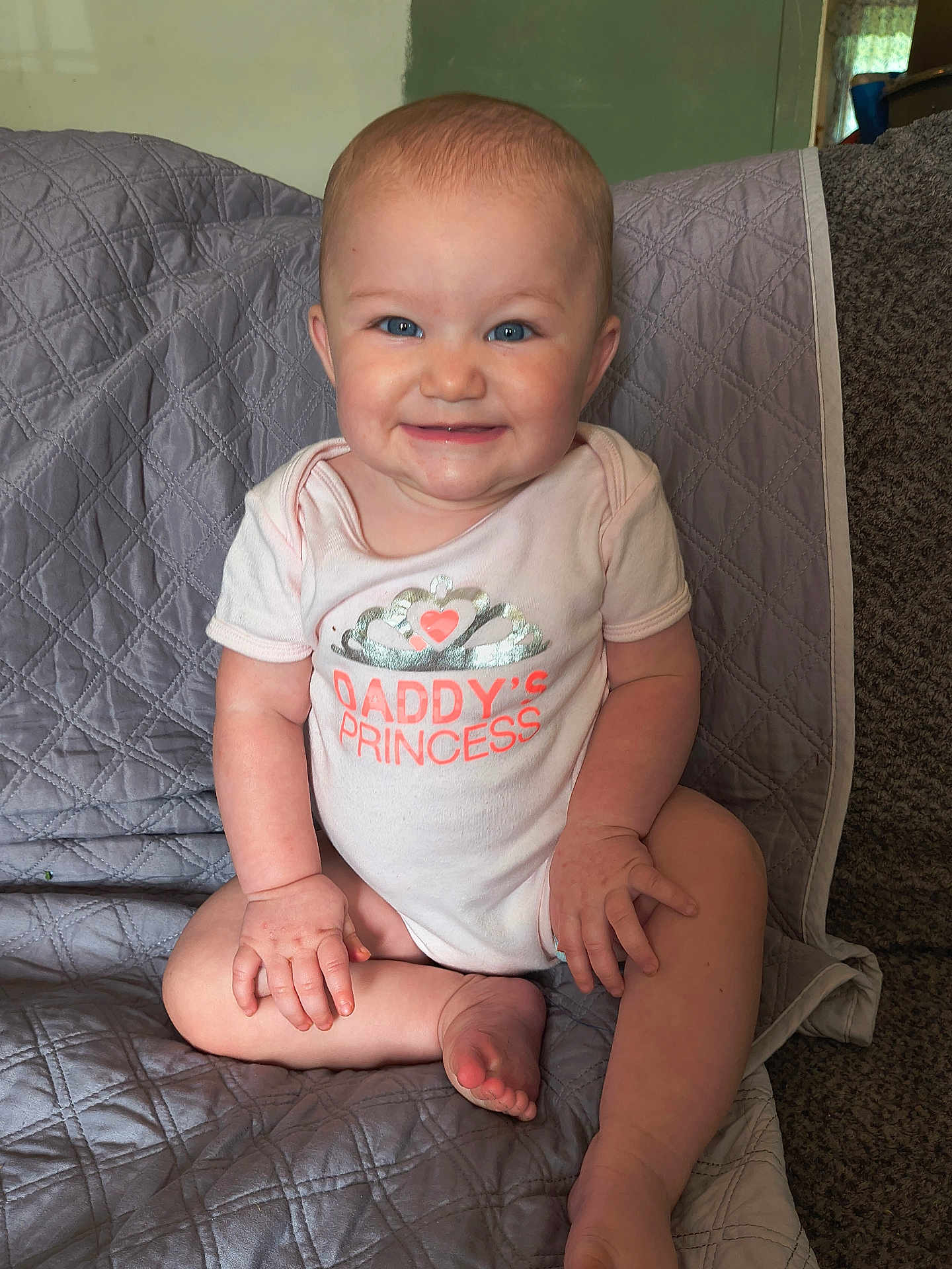 Harley is registered to the contest to win money with this photo: baby, child, infant, smile, onesie, sitting, blue_eyes, face, hands, feet, quilted_blanket, gray_blanket, indoors, cute, happy, portrait, tiara_graphic, daddys_princess, candid, skin