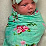 baby, newborn, infant, swaddle_blanket, headband, bow, floral_pattern, mint_green, pink, wrapped, portrait, close_up, rosy_cheeks, sleepy, cute, adorable, soft_texture, bedding, blanket, nursery
