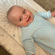 Ollie joined the competition — help win amazing prizes! baby, smiling, infant, blue_sweater, lying_down, baby_mat, patterned_mat, happy, cute, child, face, skin, hand, cozy, indoor, portrait, soft_light, carpet, closeup, head