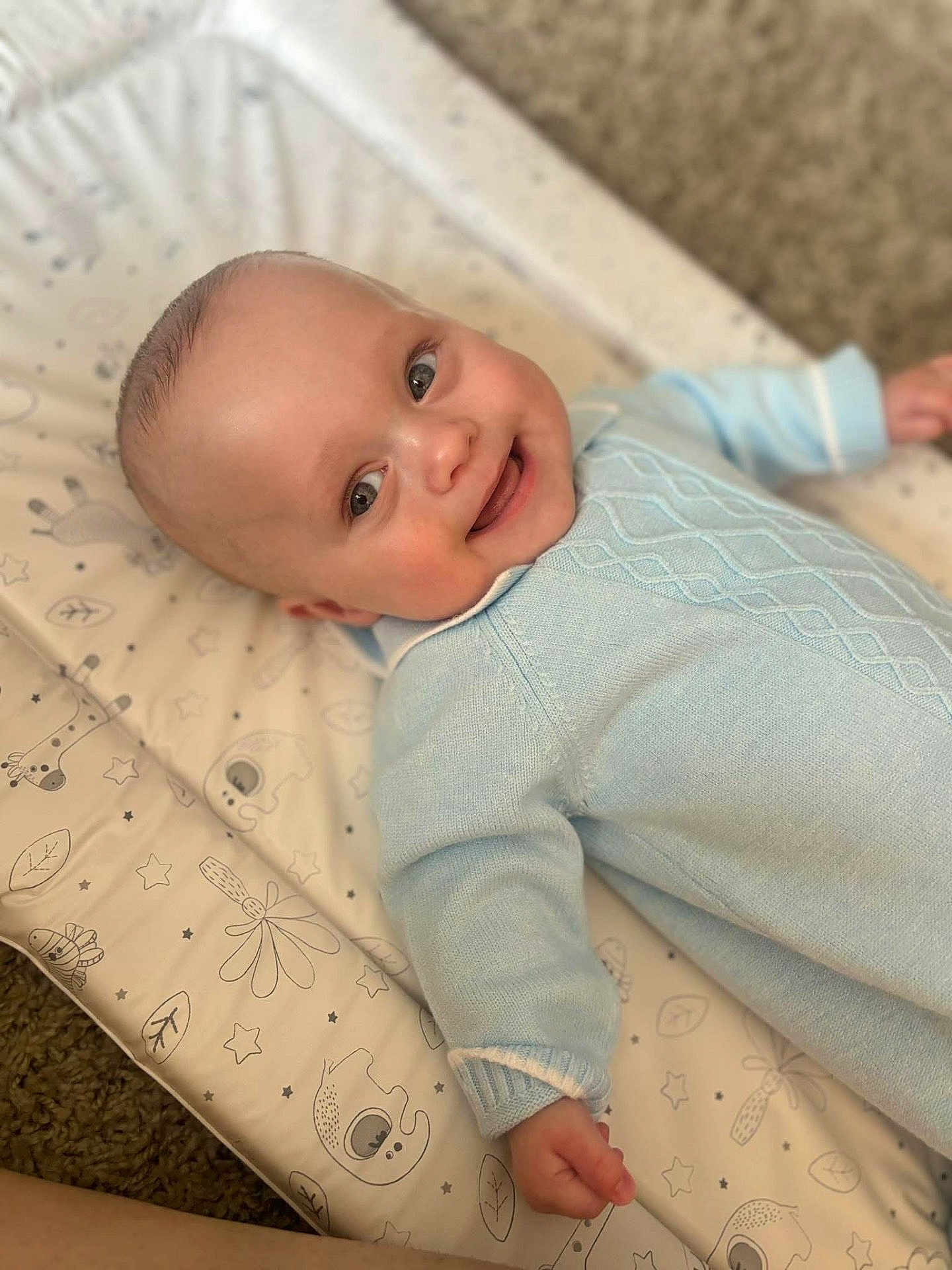 Ollie joined the competition — help win amazing prizes! baby, smiling, infant, blue_sweater, lying_down, baby_mat, patterned_mat, happy, cute, child, face, skin, hand, cozy, indoor, portrait, soft_light, carpet, closeup, head