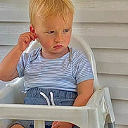 Alan a rejoint le concours — aidez-le/la à gagner de superbes lots ! toddler, child, high_chair, striped_shirt, blue_shorts, serious_expression, scratching_ear, white_wall, green_vent, paper_bag, indoor, furniture, person, seated, short_hair, casual_clothing, young_child, contemplative, blond_hair, portrait