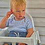 toddler, child, high_chair, striped_shirt, blue_shorts, serious_expression, scratching_ear, white_wall, green_vent, paper_bag, indoor, furniture, person, seated, short_hair, casual_clothing, young_child, contemplative, blond_hair, portrait
