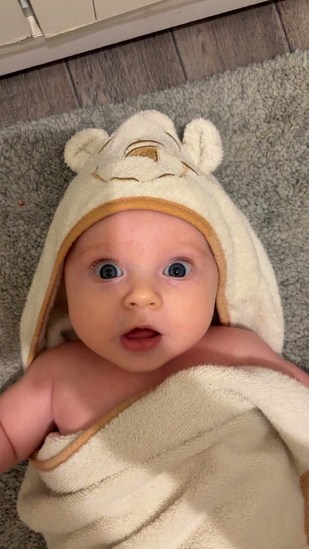 Charlotte joined the competition — help win amazing prizes! baby, towel, hood, face, eyes, expression, blanket, skin, infant, child, floor, wooden_floor, carpet, cute, indoor, portrait, person, soft_texture, wrapped, young