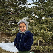 Jorawar joined the competition — help win amazing prizes! child, smiling, outdoor, winter_clothing, hat, jacket, trees, evergreen, snow, grass, nature, person, young, cute, cold_weather, green_pants, standing, happy, face, portrait