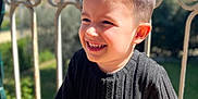 Naël a rejoint le concours — aidez-le/la à gagner de superbes lots ! background_blur, black_clothing, boy, casual_wear, cheerful, child, daylight, face, greenery, happy, nature, outdoor, person, portrait, railing, short_hair, smiling, sunlight, sweater, young