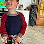 child, boy, smiling, indoor, sweater, pacifier, toy, plush_toy, living_room, floor, speaker, door, photo_frame, television, hair, person, clothing, marble_floor, furniture, decor