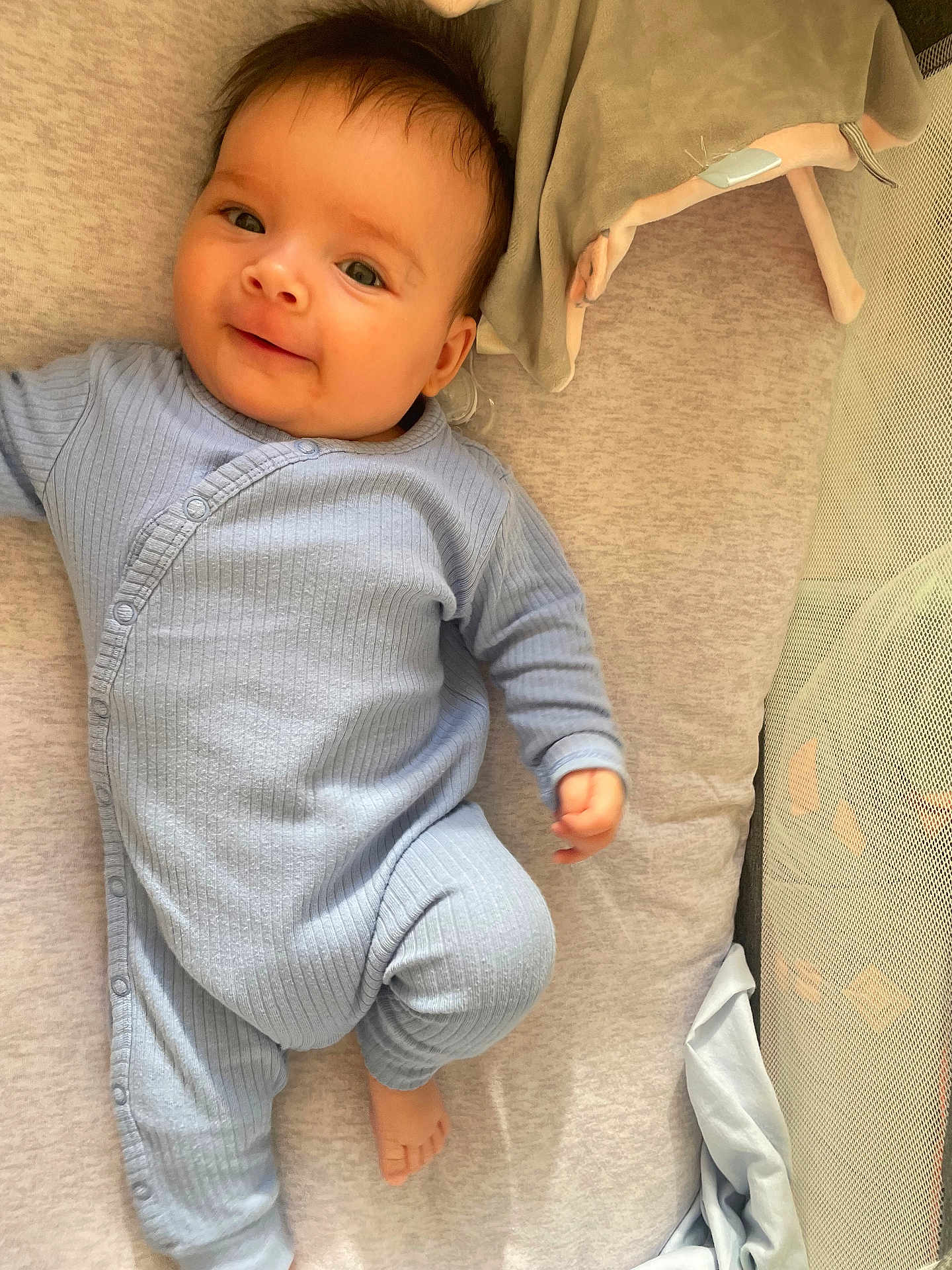 Gohana participe au concours pour gagner de l'argent avec cette photo : baby, infant, smile, blue_onesie, bed, bedding, soft_toy, cute, child, lying_down, indoors, portrait, happy, young, face, skin, hands, feet, cozy, sleeping_area