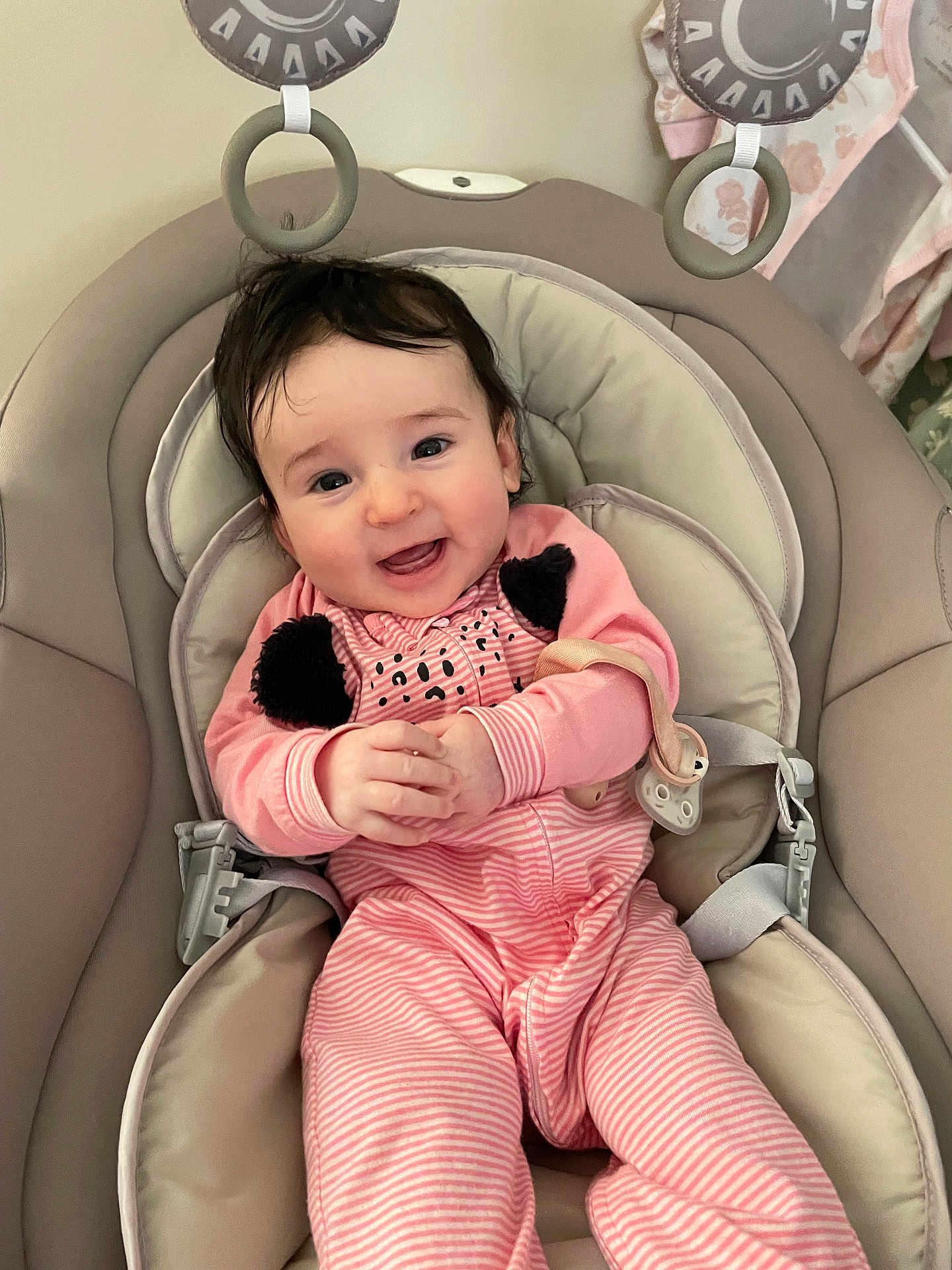Emerson is registered to the contest to win money with this photo: baby, infant, smiling, pink_clothing, onesie, baby_seat, toy_rings, happy, cute, child, indoor, portrait, young_child, seat_belt, soft_toys, clasped_hands, comfortable, head, face, expression