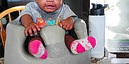 Miracle Cheatham is registered to the contest to win money with this photo: baby, infant, child, face, smile, baby_seat, socks, shirt, table, water_bottle, plastic_bag, chair, indoor, expression, cute, person, furniture, patterned_tablecloth, eyes, hand
