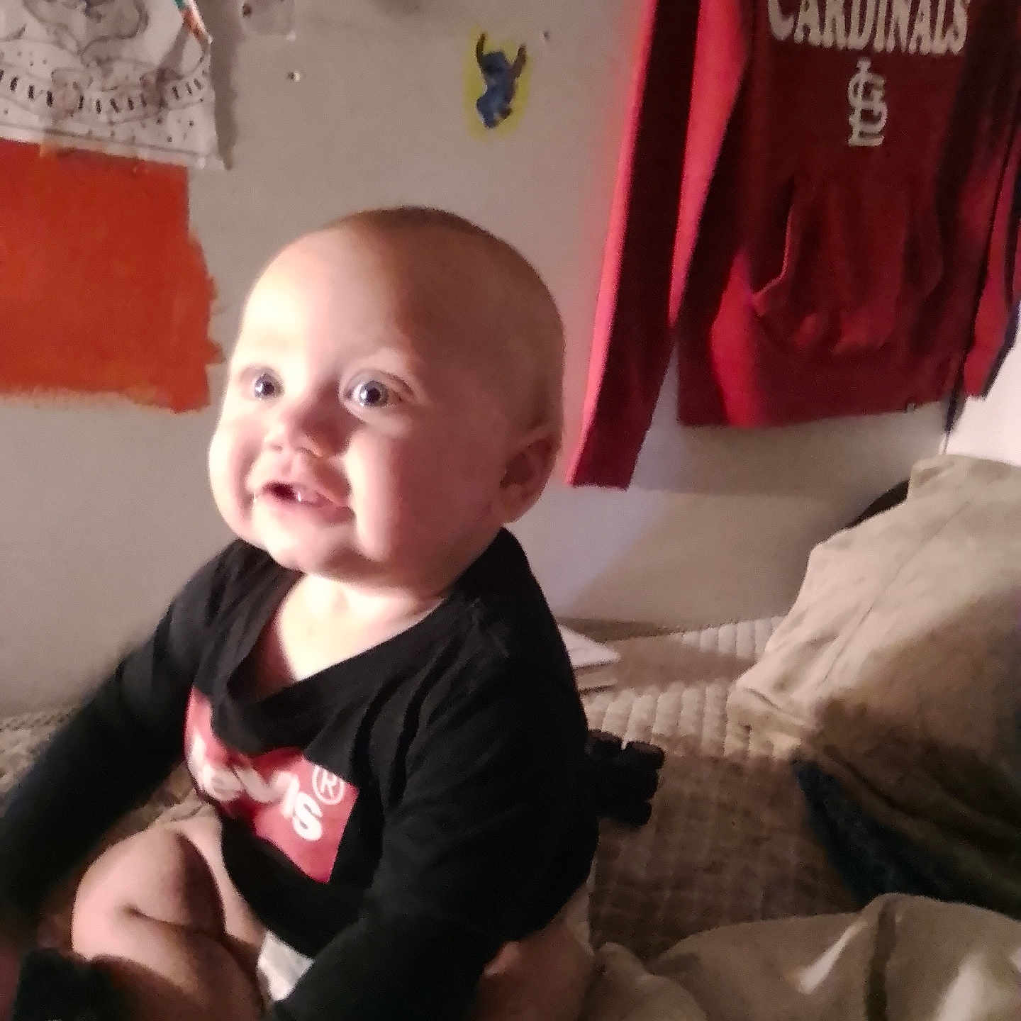 Drakken is registered to the contest to win money with this photo: baby, child, infant, smiling, happy, portrait, sitting, bed, bedroom, indoors, clothing, black_shirt, face, eyes, head, skin, blanket, pillow, wall, laundry