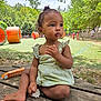 toddler, child, outdoor, park, playground, greenery, trees, picnic_table, dress, food, sitting, baby, face, hand, foot, daylight, nature, curly_hair, expression, bench