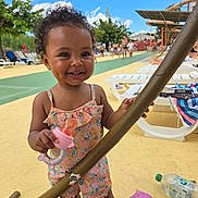 Diana participe au concours pour gagner de l'argent avec cette photo : toddler, child, smiling, pacifier, curly_hair, outdoor, summer, sunny, playground, lounge_chair, pool_area, happy, dimple, clothing, person, toy, barefoot, trees, blue_sky, people