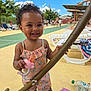 toddler, child, smiling, pacifier, curly_hair, outdoor, summer, sunny, playground, lounge_chair, pool_area, happy, dimple, clothing, person, toy, barefoot, trees, blue_sky, people