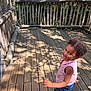 Leya participe au concours pour gagner de l'argent avec cette photo : child, toddler, curly_hair, smiling, wooden_deck, wooden_fence, outdoor, sunlight, shadow, striped_shirt, denim_shorts, sneakers, playful, happy, nature, daylight, person, summer, casual_clothing, walking