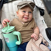 Bodhi joined the competition — help win amazing prizes! baby, child, stroller, cap, blue_eyes, blanket, sippy_cup, clothing, denim_shorts, smile, hand, face, infant, cute, portrait, person, outdoor, seat, fabric, relaxing