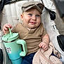 baby, child, stroller, cap, blue_eyes, blanket, sippy_cup, clothing, denim_shorts, smile, hand, face, infant, cute, portrait, person, outdoor, seat, fabric, relaxing