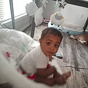 Josiah joined the competition — help win amazing prizes! baby, infant, child, sitting, portrait, face, eyes, curious, indoors, nursery, baby_mobile, stuffed_animal, cushion, white_clothing, dog, pet, wood_floor, window, daylight, home
