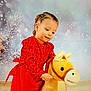 background, celebration, child, cute, decorations, festive, girl, happy, holiday, holiday_theme, indoor, playful, plush_toy, portrait, red_dress, smiling, snowflakes, toy_horse, winter, young_child