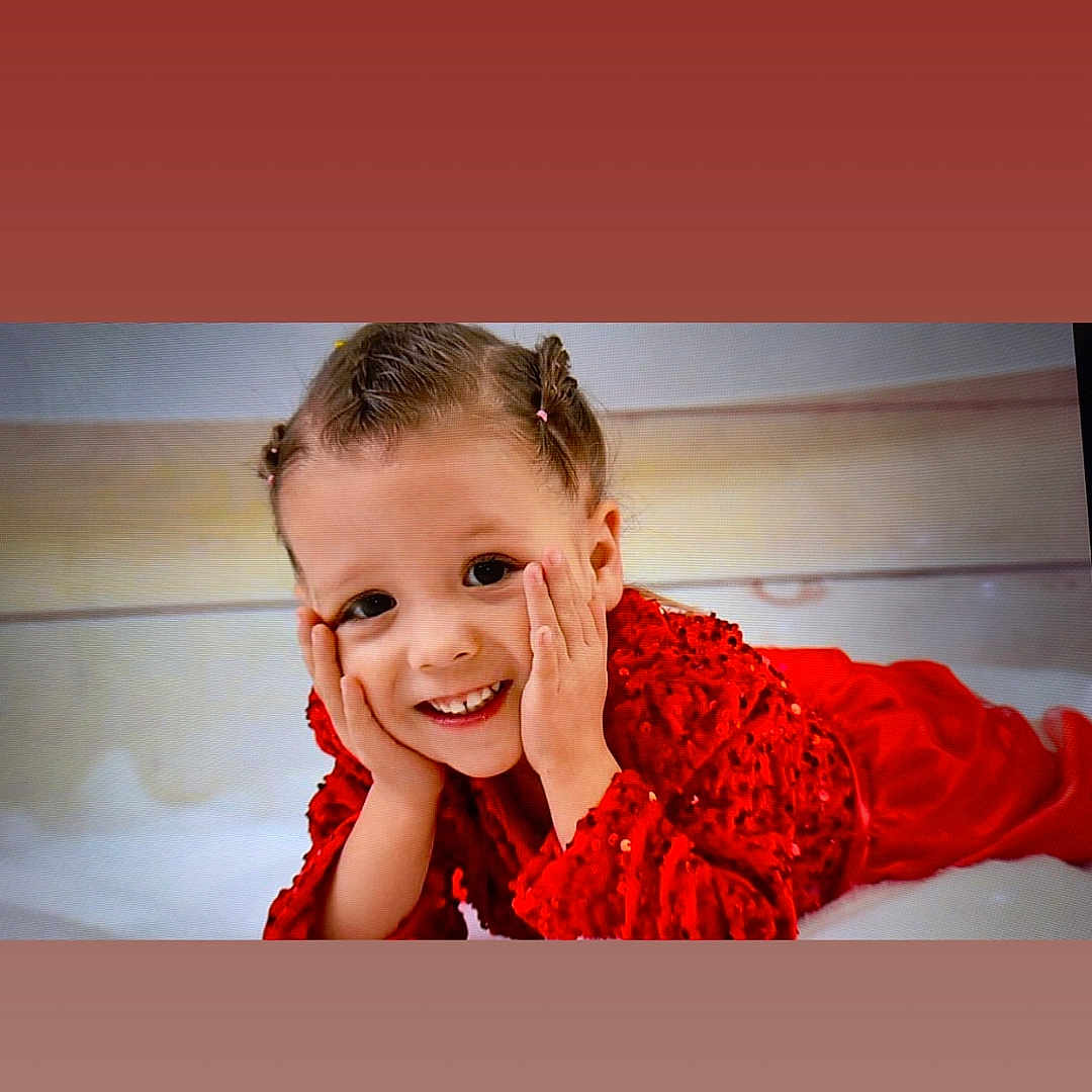 Ylonna a rejoint le concours — aidez-le/la à gagner de superbes lots ! bright, child, closeup, cute, expression, face, fashion, hair_tied, hands, happy, indoors, joyful, lying_down, person, playful, portrait, red_clothing, sequin, smiling, young_child