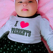 Mia is registered to the contest to win money with this photo: baby, infant, headband, bow, tongue, shirt, text, polka_dot, skirt, pink_blanket, lying_down, cute, child, adorable, clothing, portrait, face, person, indoors, smiling