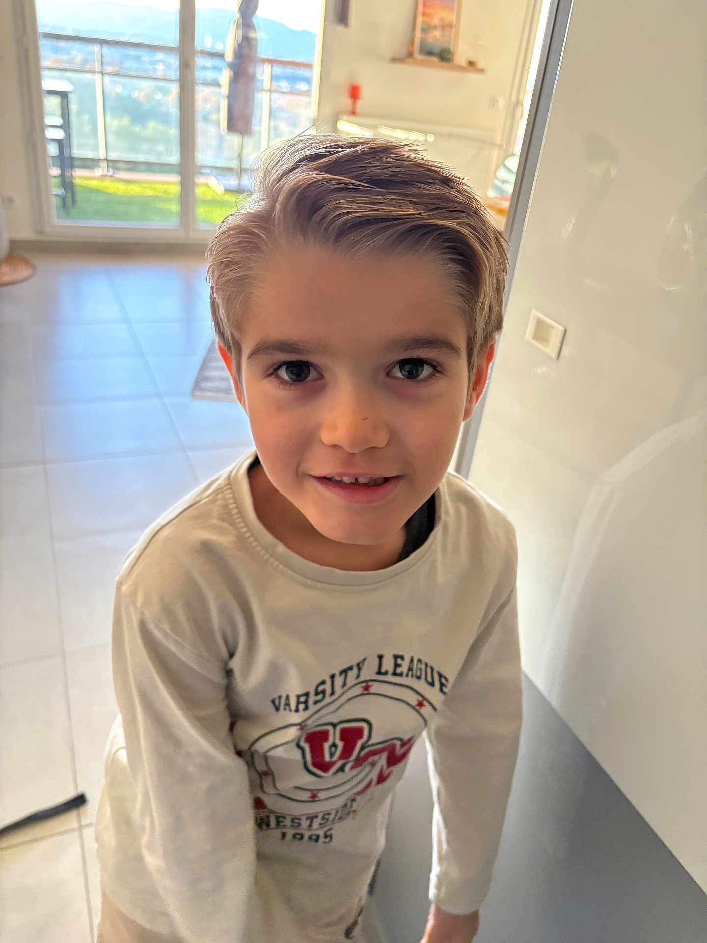 Mathys a rejoint le concours — aidez-le/la à gagner de superbes lots ! child, boy, indoor, portrait, smiling, casual_clothing, long_sleeve_shirt, hair, face, eyes, tile_floor, balcony, window, daylight, home_interior, wall, light_switch, young, person, standing