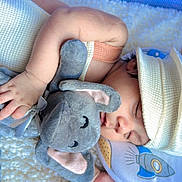 Ethan is registered to the contest to win money with this photo: baby, sleeping, plush_toy, elephant, hat, blanket, pillow, rocket, infant, cute, soft, cozy, child, peaceful, hand, face, indoors, rest, comfort, adorable