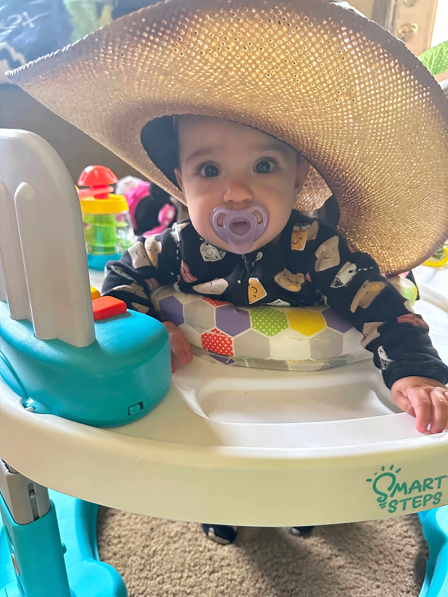 Ivory is registered to the contest to win money with this photo: baby, pacifier, hat, baby_walker, toy, indoor, child, face, clothing, hand, carpet, person, cute, playful, colorful, infant, expression, soft_light, home, smile