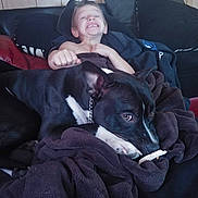 Capone is registered to the contest to win money with this photo: child, dog, black_dog, blanket, couch, happy, smiling, indoor, relaxed, comfort, pet, furniture, canine, portrait, casual, cozy, resting, home, friendship, playful