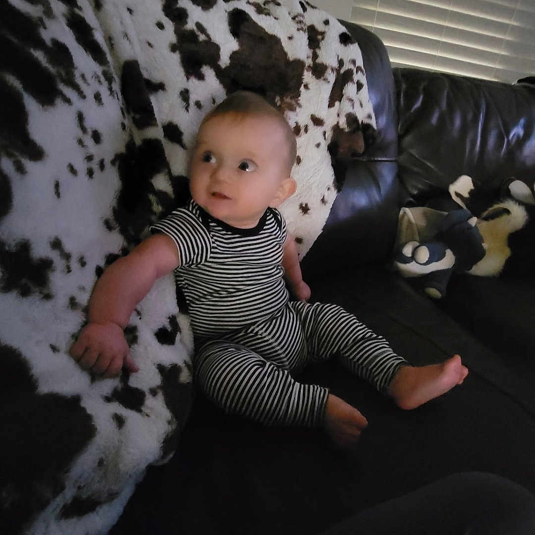 Hayes joined the competition — help win amazing prizes! baby, striped_clothing, couch, blanket, leather_furniture, indoor, child, window_blinds, plush_toys, curious, seated, striped_pajamas, infant, living_room, soft_lighting, home, person, face, foot, hand