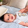 Elio is registered to the contest to win money with this photo: baby, infant, smiling, onesie, teddy_bear, blanket, bed, cute, happy, child, indoor, soft, legs, face, skin, head, person, young, cozy, comfort
