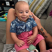 Matteo Ace is registered to the contest to win money with this photo: baby, blanket, child, clothing, couch, face, hand, happy, home, indoor, infant, legs, person, pillow, relaxation, shirt, shorts, sitting, smile, tattoo
