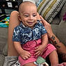 baby, blanket, child, clothing, couch, face, hand, happy, home, indoor, infant, legs, person, pillow, relaxation, shirt, shorts, sitting, smile, tattoo