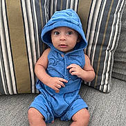 Matteo Ace is registered to the contest to win money with this photo: baby, child, blue_clothing, hood, whale_print, couch, striped_pillows, gray_fabric, sitting, curious_expression, indoors, infant, cute, casual_wear, portrait, small_hands, bare_legs, comfortable, soft_lighting, relaxed