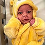 baby, infant, yellow_outfit, hood, crown, plush, soft_texture, close_up, cute, face, eyes, hand, furniture, bed, blanket, indoor, portrait, child, newborn, cozy