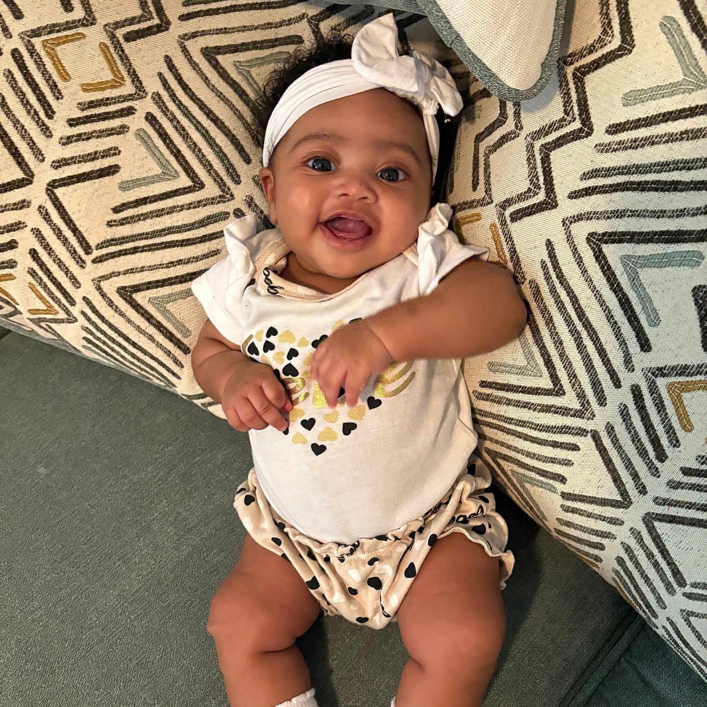 Keani joined the competition — help win amazing prizes! baby, cheerful, child, closeup, couch, cozy, cushion, cute, happy, headband, indoor, infant, patterned_clothing, person, playful, portrait, sitting, smiling, soft_fabric, white_socks