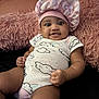 baby, infant, child, pink_bonnet, onesie, cloud_pattern, fluffy_pillow, smiling, cute, chubby_cheeks, indoor, portrait, cozy, relaxed, person, furniture, soft_texture, headwear, happy, skin